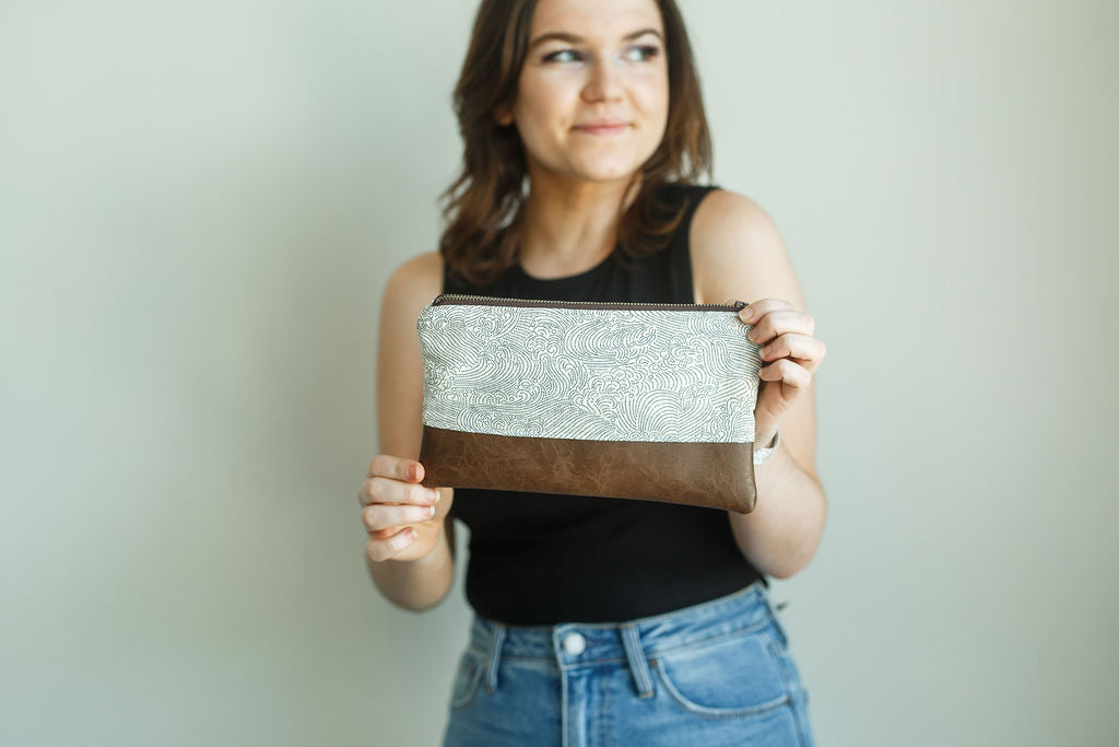 woman holding a wristlet. fabric is white with blue waves and a brown vinyl bottom