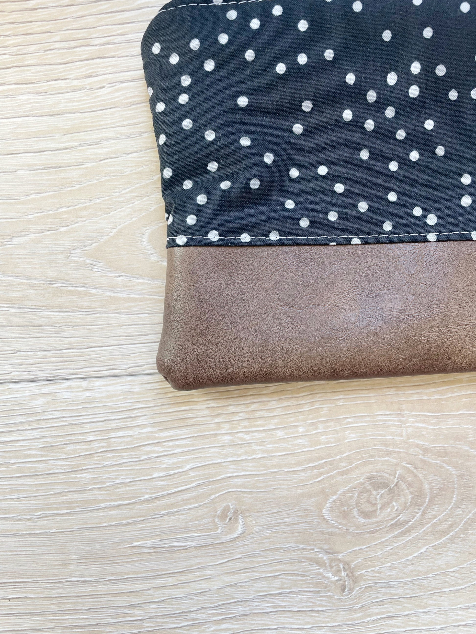 black and gray dot wristlet with silver zipper and brown vinyl along bottom of clutch. matching black and gray dot wrist strap