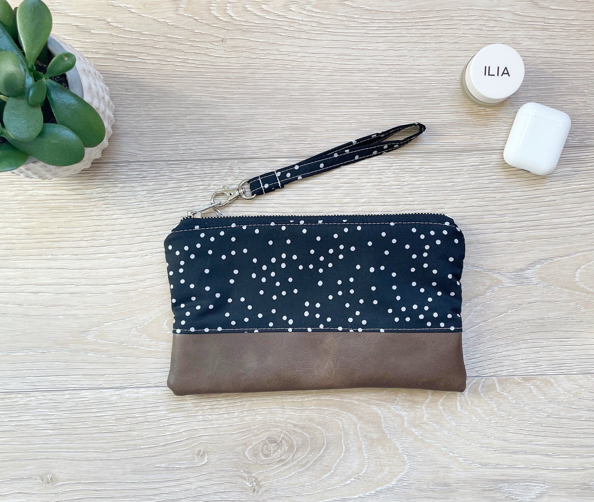 black and gray dot wristlet with silver zipper and brown vinyl along bottom of clutch. matching black and gray dot wrist strap
