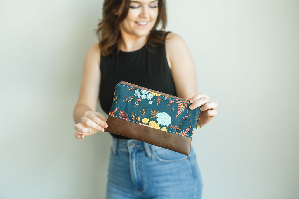 floral and fern navy wristlet with matching wrist strap and brown vinyl along the bottom. antique brass zipper. 