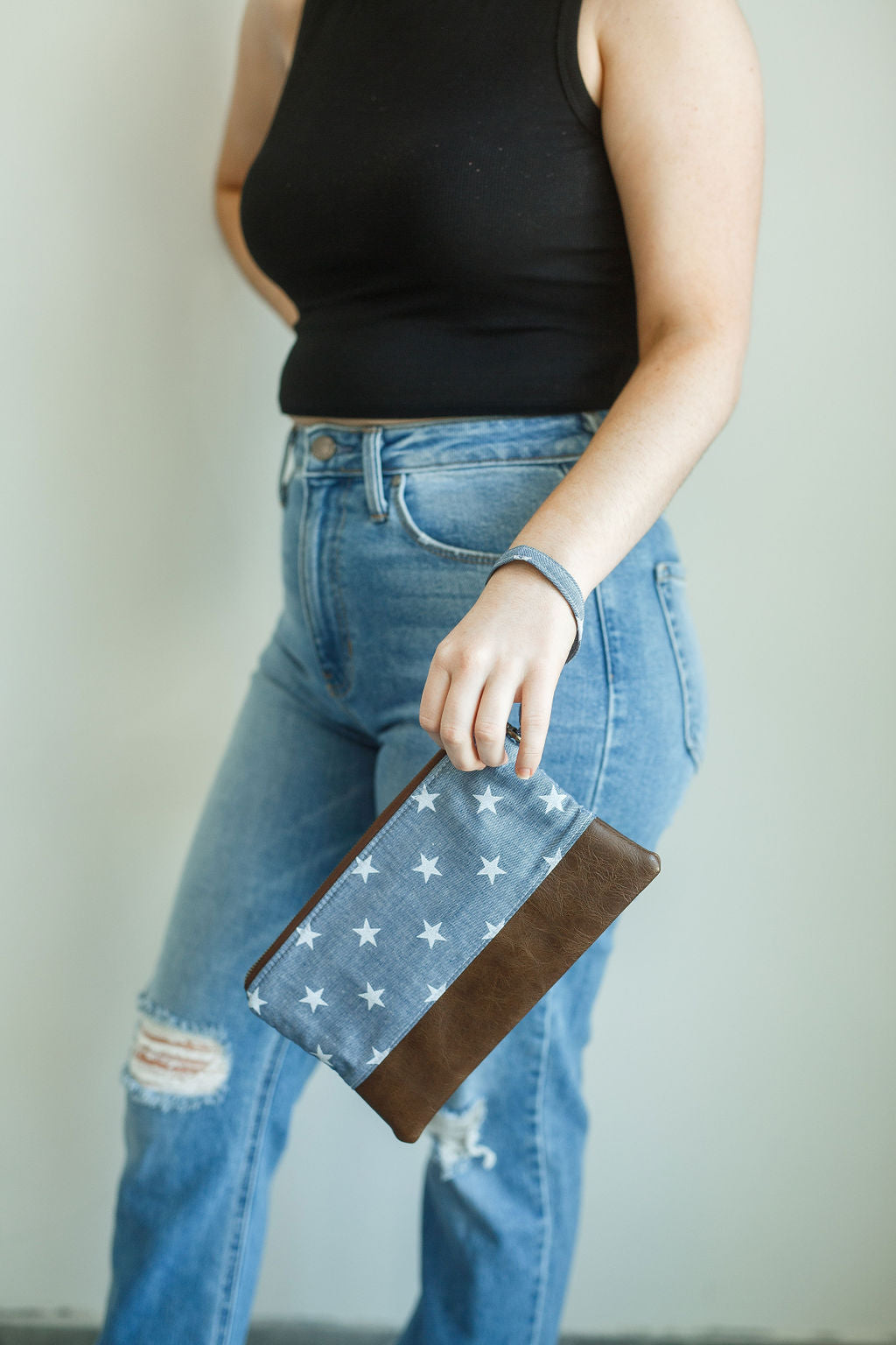 chambray wristlet with white stars and matching wrist strap. brown vinyl along the bottom and antique brass zipper