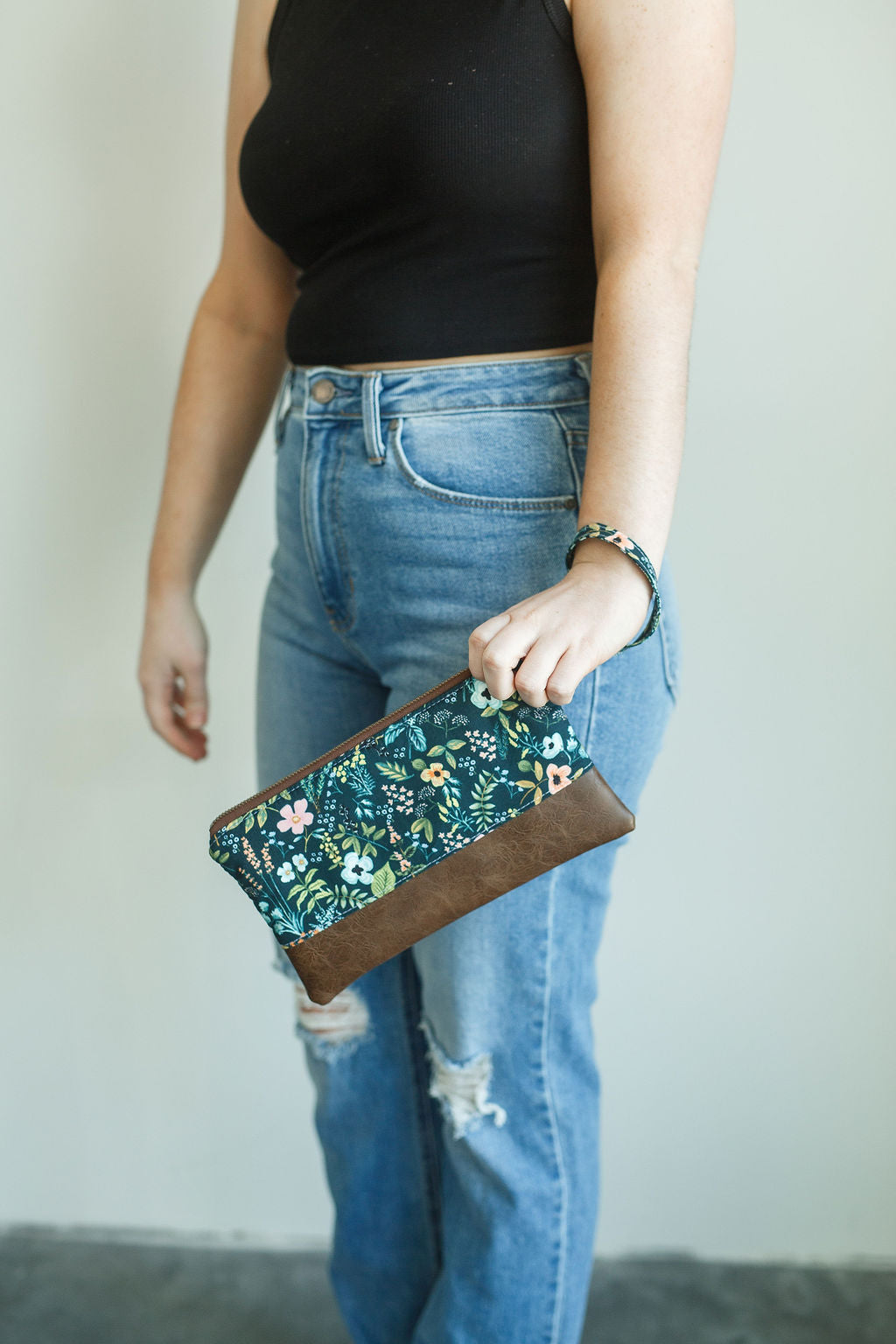 Blue floral wristlet with pink flowers and brown vinyl along the bottom. wristlet has matching wrist strap and antique brass zipper