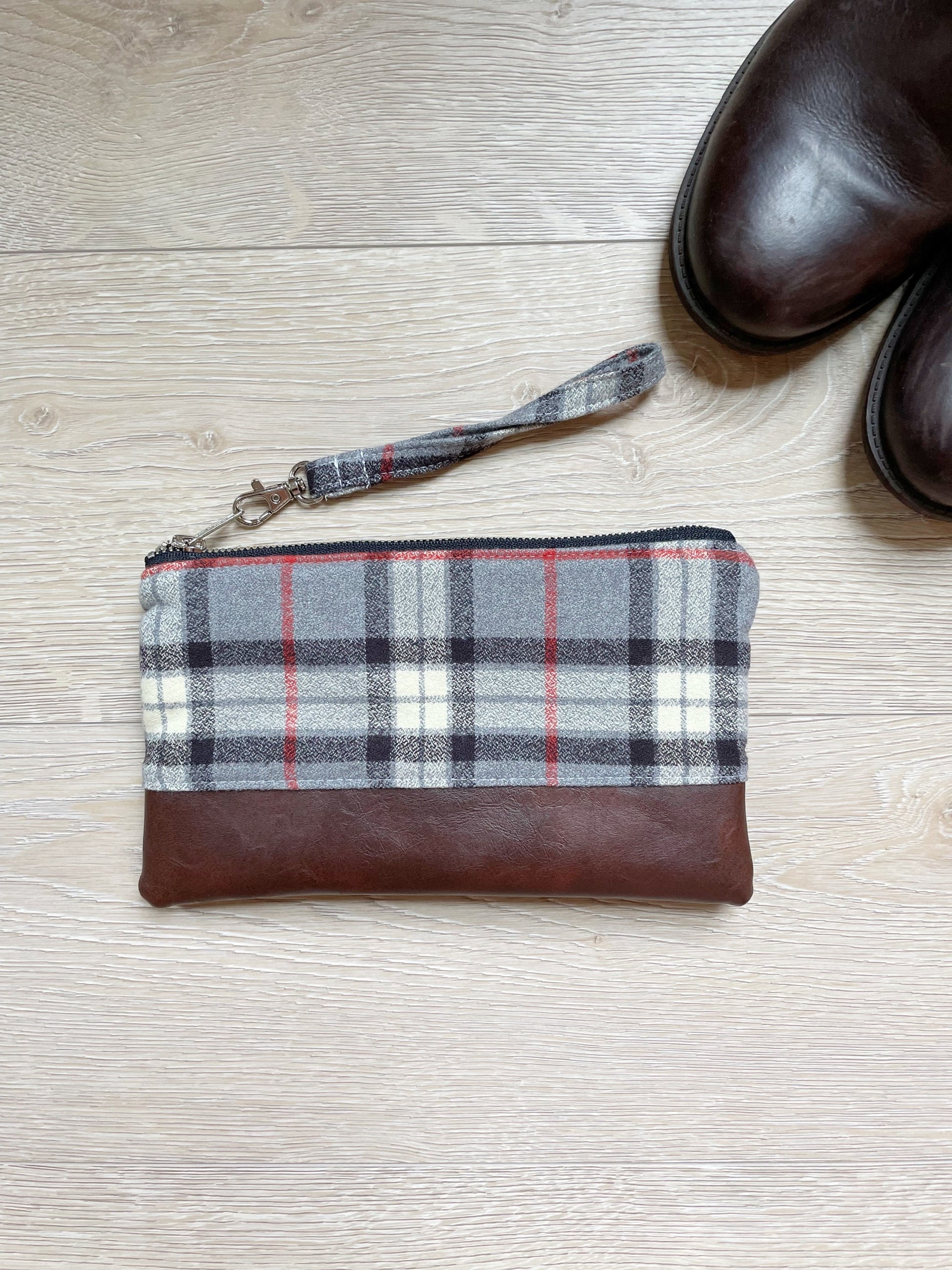 Black gray red and white flannel wristlet with brown vinyl along the bottom. Matching wrist strap and silver zipper