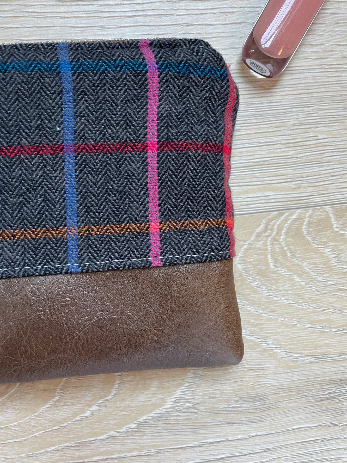 colorful charcoal plaid flannel wristlet with matching wrist strap and brown vinyl along the bottom.
