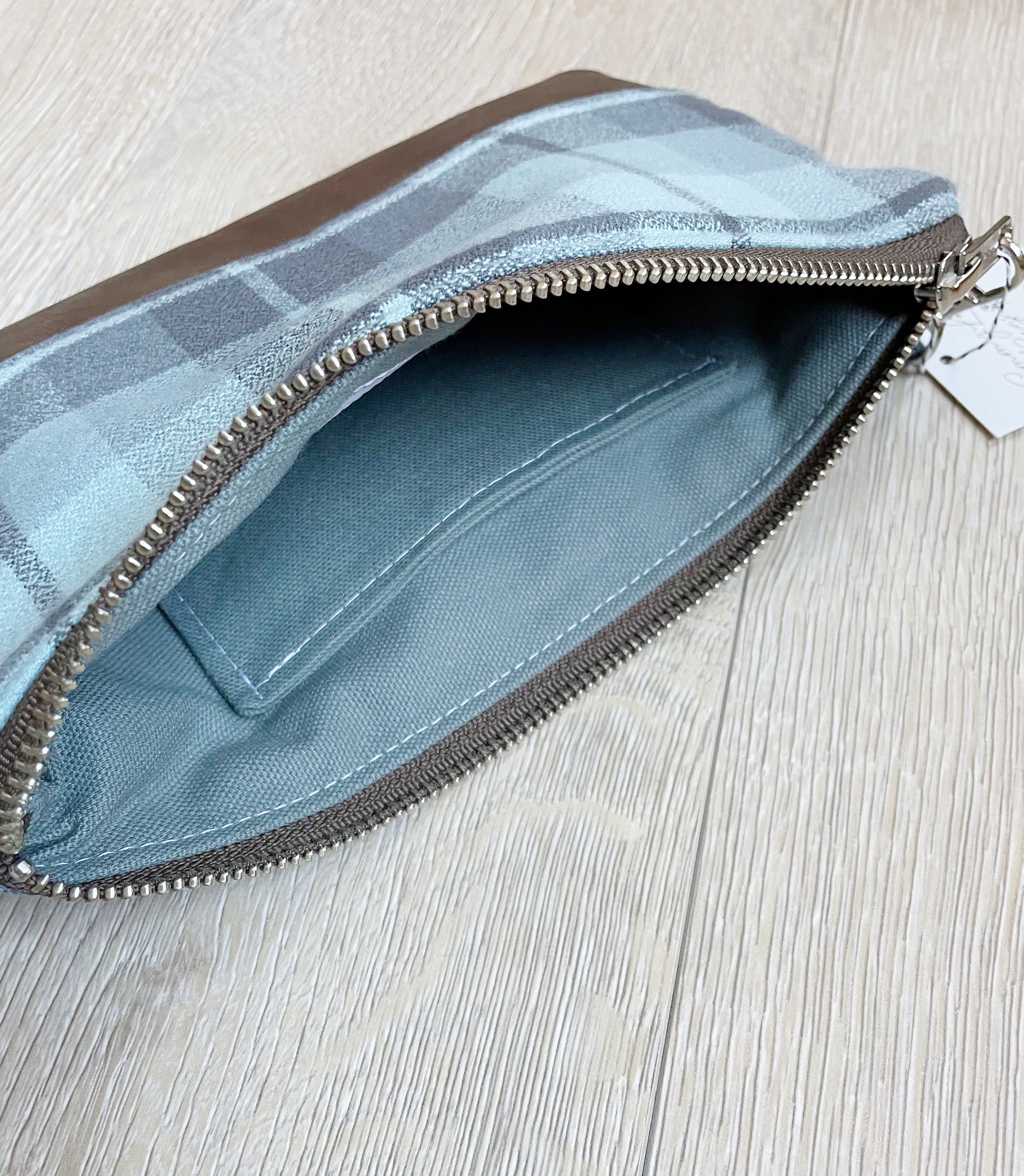 Blue and gray flannel wristlet with brown vinyl along the bottom, closed with a silver zipper. matching flannel wrist strap. lining is gray with a slip pocket for cards