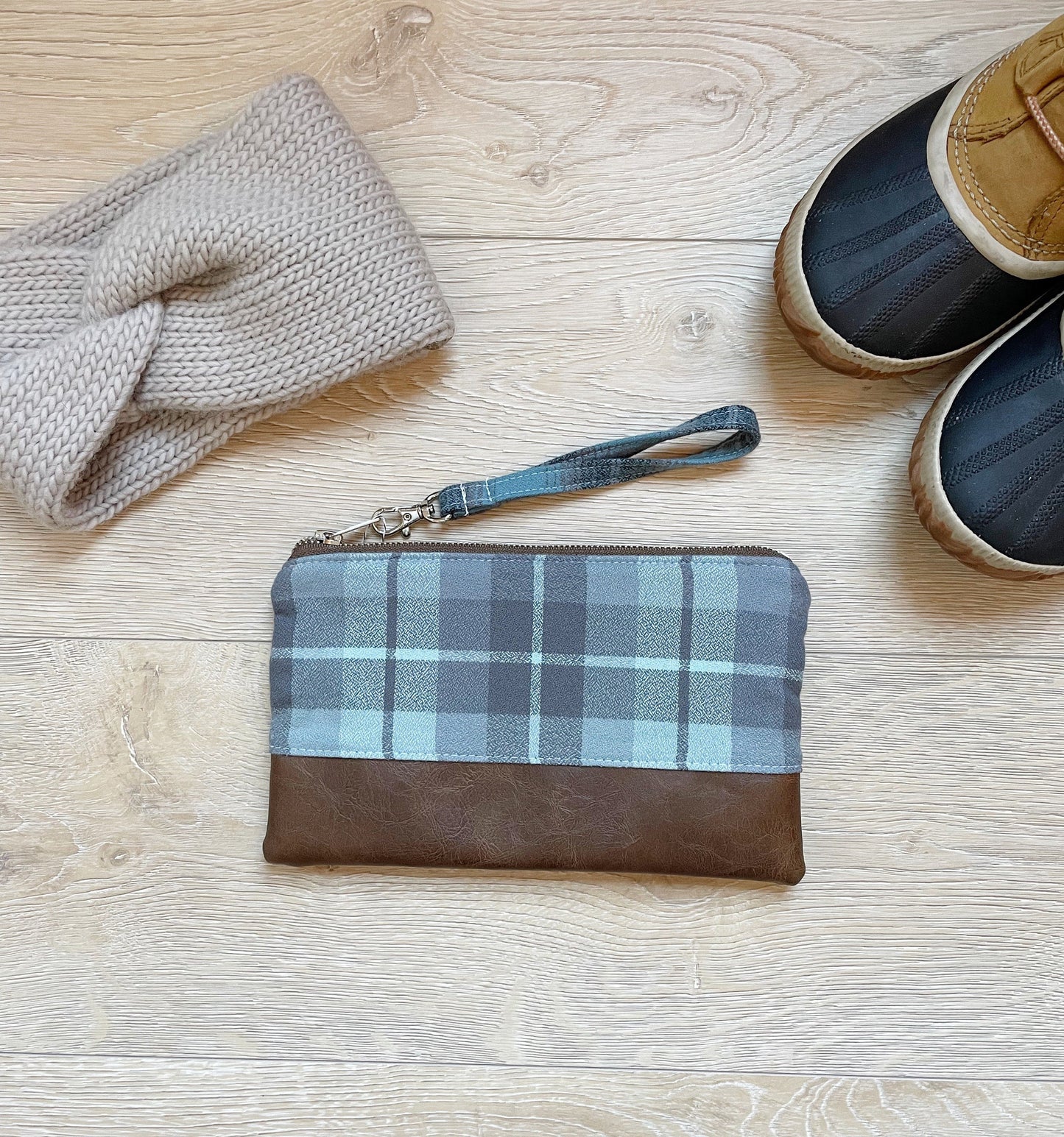 Blue and gray flannel wristlet with brown vinyl along the bottom, closed with a silver zipper. matching flannel wrist strap