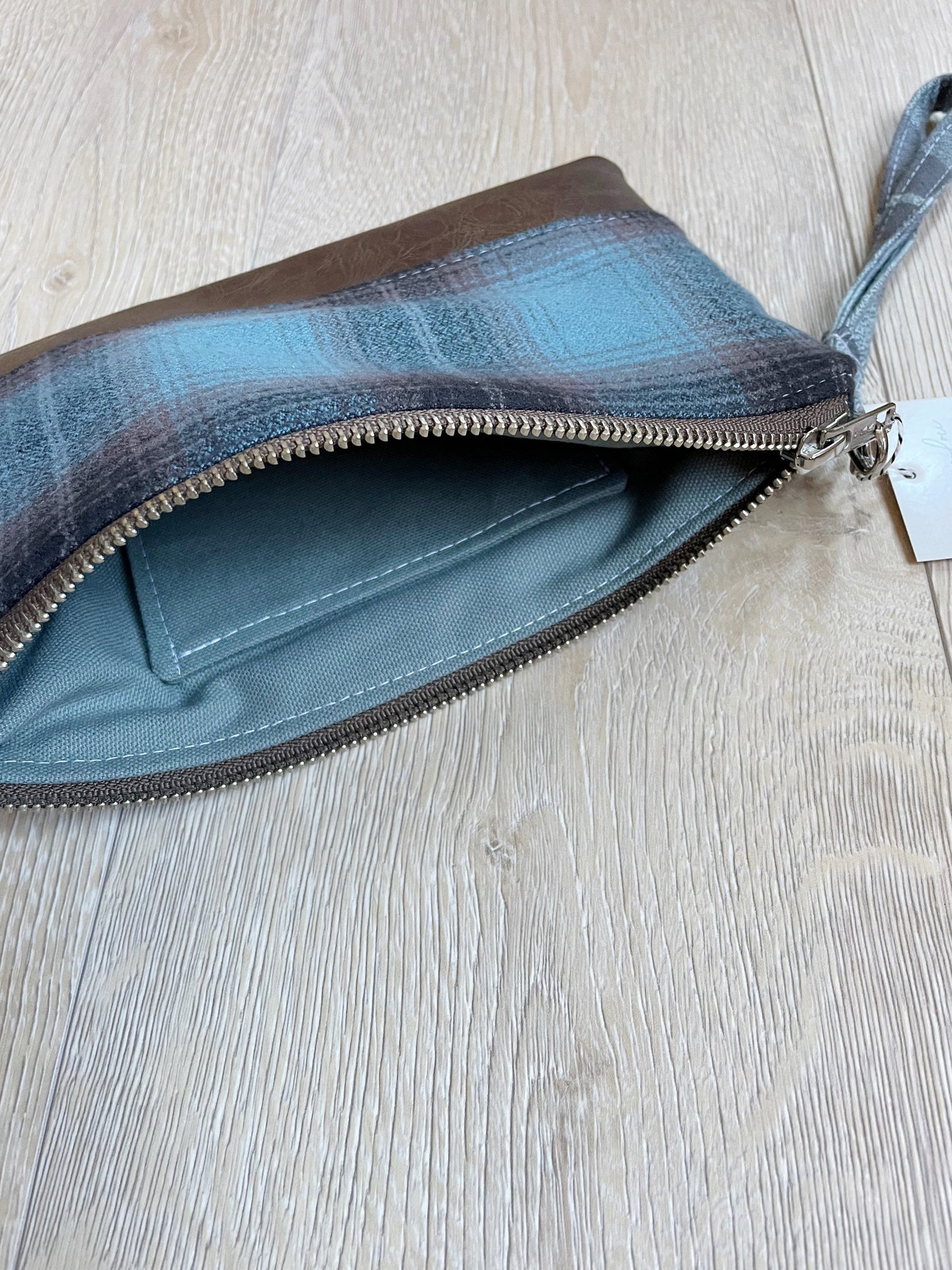 blue black and brown flannel wristlet with brown vinyl bottom. matching wrist strap. gray lining with slip pocket for cards 
