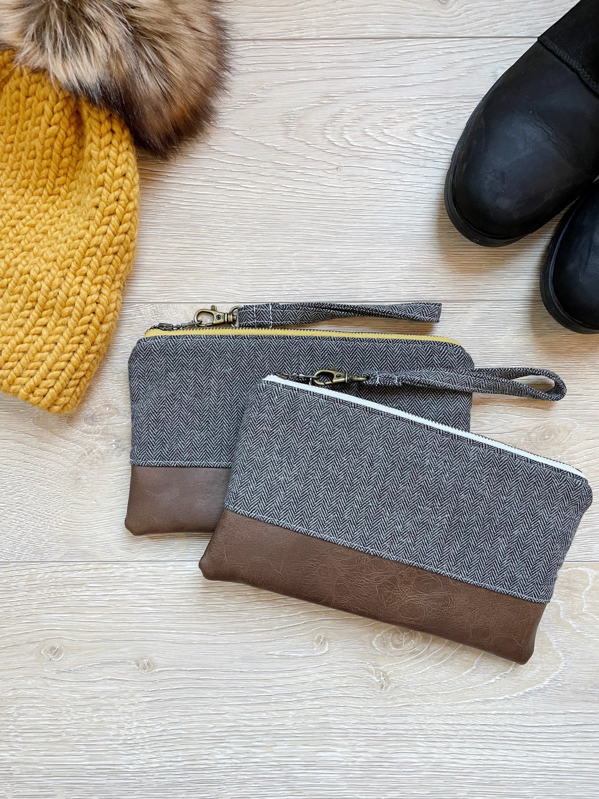 gray herringbone flannel wristlet with matching wrist strap and brown vinyl along the bottom. 